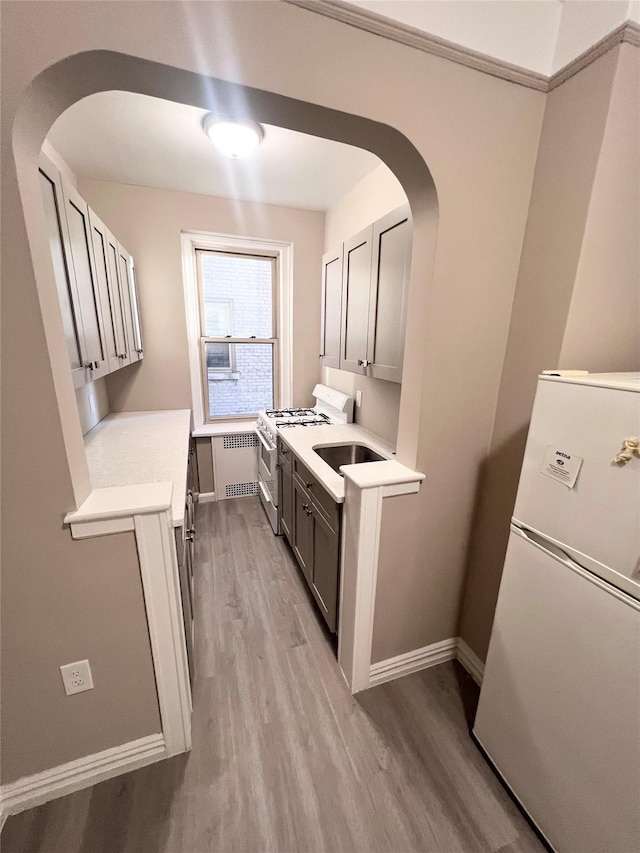 kitchen featuring gray cabinets, light wood-type flooring, radiator heating unit, and white appliances