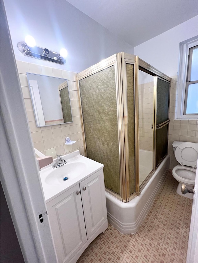 full bathroom featuring enclosed tub / shower combo, vanity, toilet, and tile walls