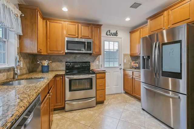 kitchen with light tile patterned flooring, sink, light stone counters, tasteful backsplash, and appliances with stainless steel finishes