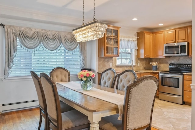 dining area with sink, a baseboard heating unit, a notable chandelier, light hardwood / wood-style floors, and ornamental molding