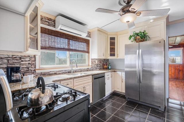 kitchen featuring dark tile patterned flooring, cream cabinets, stainless steel appliances, a wall mounted AC, and a sink