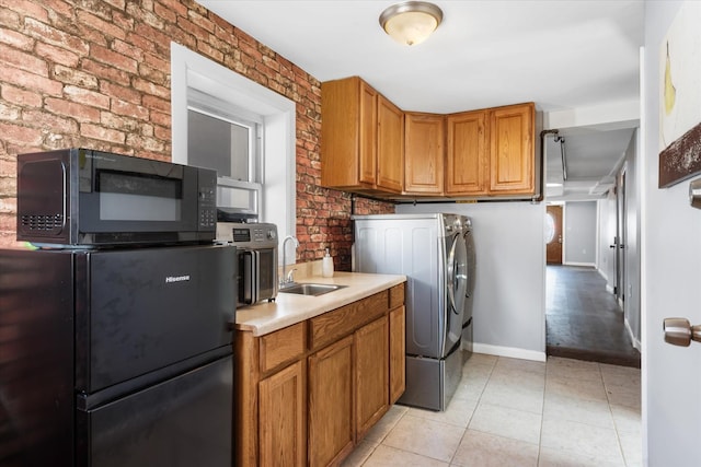 laundry area with a sink, washer / clothes dryer, brick wall, light tile patterned flooring, and baseboards