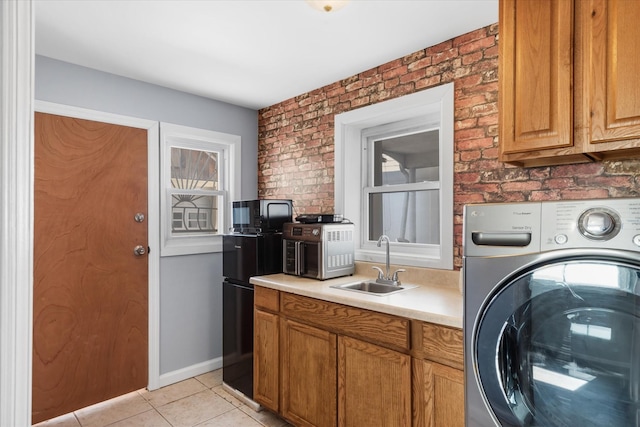 laundry area featuring light tile patterned floors, brick wall, laundry area, washer / clothes dryer, and a sink