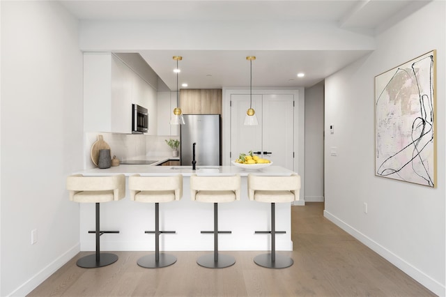 kitchen featuring hanging light fixtures, stainless steel appliances, kitchen peninsula, and a kitchen bar