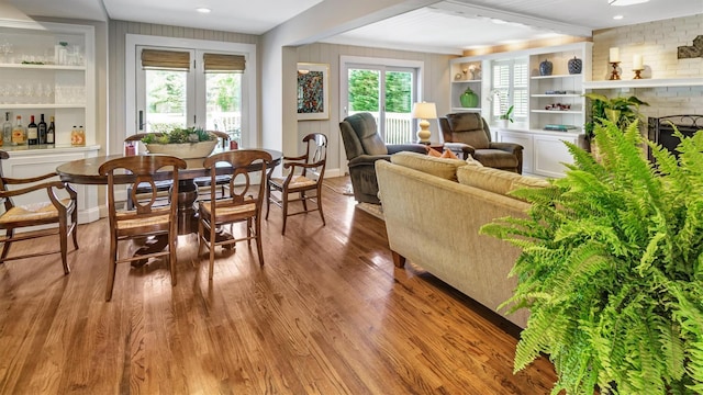 dining space with built in shelves, beam ceiling, hardwood / wood-style floors, and a brick fireplace