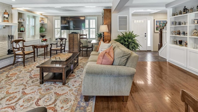 living room featuring beamed ceiling, wood-type flooring, a brick fireplace, and built in shelves