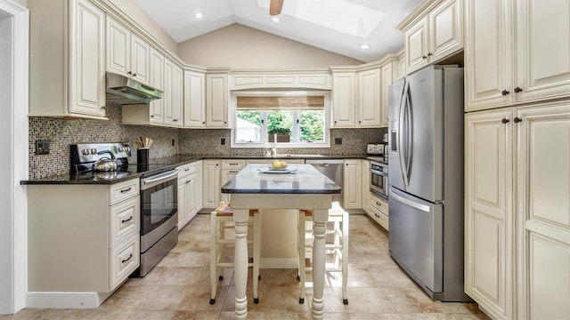 kitchen with appliances with stainless steel finishes, a kitchen breakfast bar, a center island, vaulted ceiling with skylight, and dark stone counters