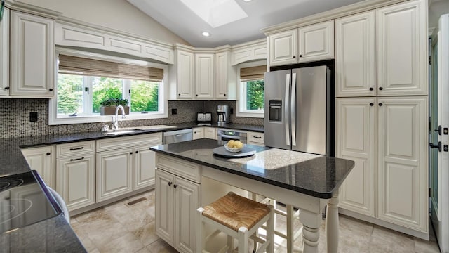 kitchen with dark stone countertops, backsplash, lofted ceiling with skylight, and appliances with stainless steel finishes