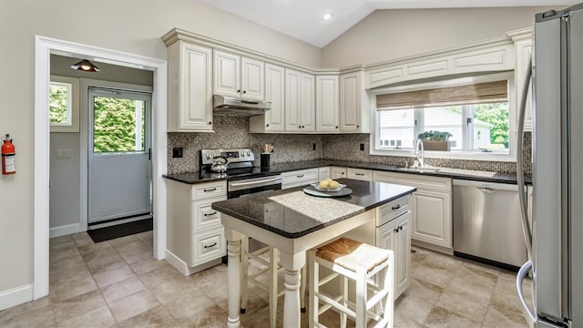 kitchen featuring vaulted ceiling, appliances with stainless steel finishes, decorative backsplash, dark stone counters, and a center island