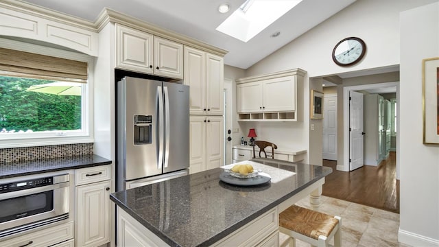 kitchen with lofted ceiling with skylight, a kitchen island, a kitchen breakfast bar, dark stone counters, and stainless steel refrigerator with ice dispenser