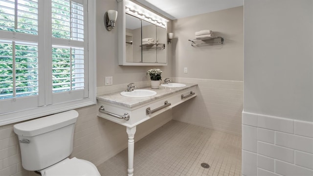 bathroom featuring toilet, dual sinks, tile walls, and a wealth of natural light