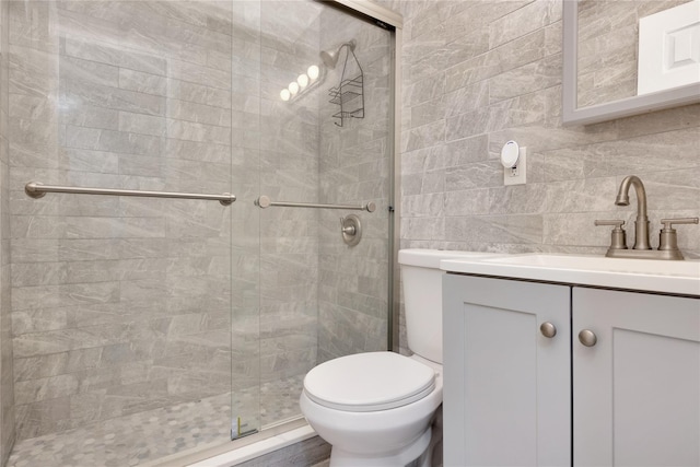 bathroom featuring tile walls, backsplash, vanity, toilet, and a shower with door