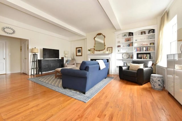 sitting room featuring built in shelves, a fireplace, light wood finished floors, and beamed ceiling