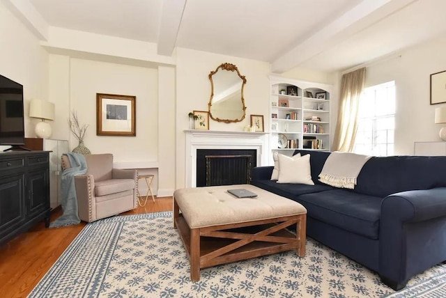 living area with a fireplace, beamed ceiling, and wood finished floors