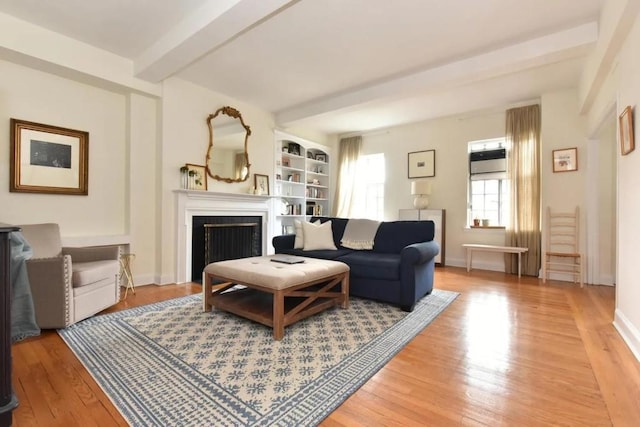 living area featuring baseboards, a fireplace, beamed ceiling, and light wood finished floors