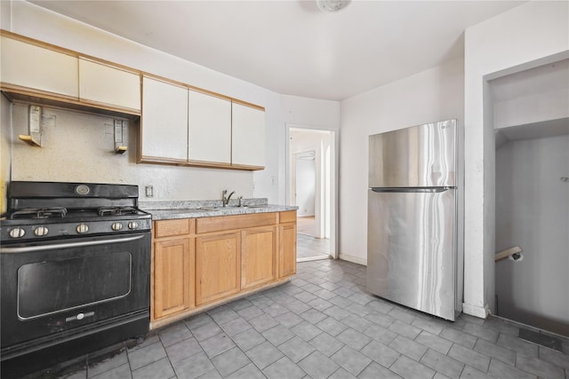 kitchen featuring black range with gas cooktop, sink, backsplash, and stainless steel refrigerator