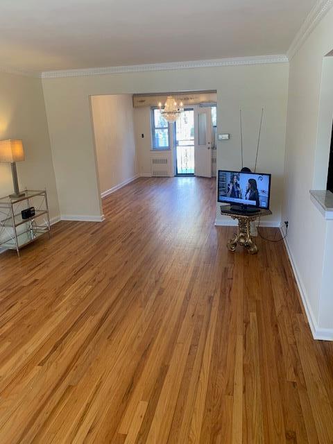 living room with an inviting chandelier, ornamental molding, wood-type flooring, and radiator heating unit