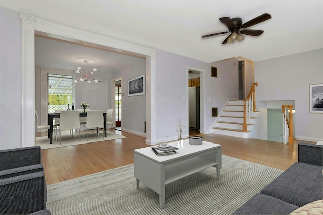 living room featuring stairs, ceiling fan with notable chandelier, light wood-type flooring, and baseboards