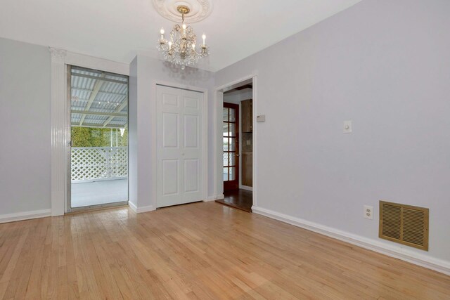 spare room featuring a chandelier, baseboards, visible vents, and light wood finished floors