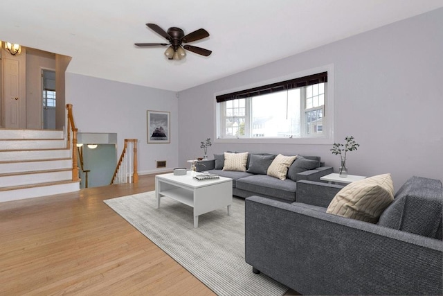 living room featuring light wood-style flooring, stairs, visible vents, and ceiling fan