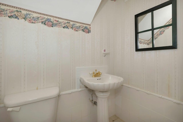 half bath featuring toilet, wallpapered walls, and a sink