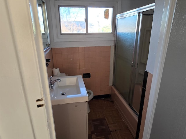 full bathroom featuring parquet flooring, toilet, tile walls, vanity, and enclosed tub / shower combo