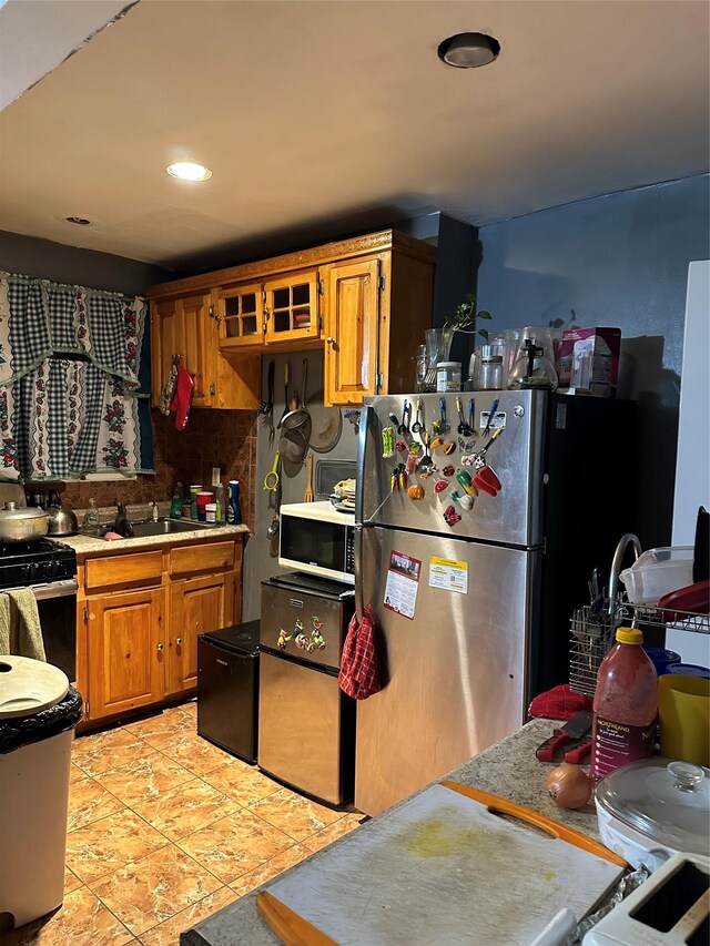 kitchen with brown cabinetry, light tile patterned flooring, a sink, stainless steel appliances, and light countertops