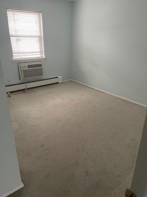 carpeted spare room featuring a wall mounted air conditioner and baseboard heating