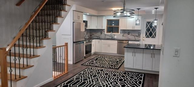 kitchen featuring appliances with stainless steel finishes, white cabinetry, sink, dark hardwood / wood-style flooring, and hanging light fixtures