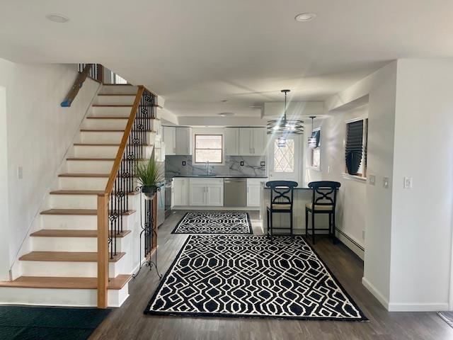 kitchen with backsplash, a baseboard heating unit, white cabinets, a sink, and dishwasher