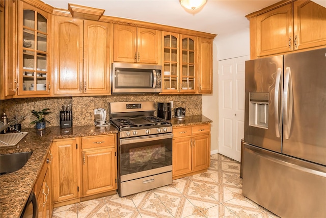 kitchen featuring dark stone counters, appliances with stainless steel finishes, backsplash, and glass insert cabinets