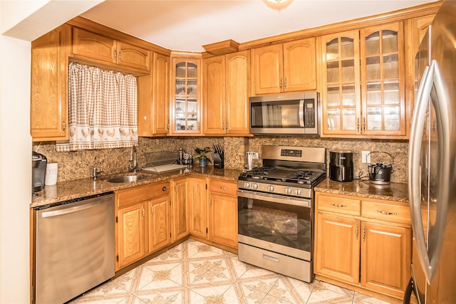 kitchen with appliances with stainless steel finishes, dark stone counters, a sink, and backsplash