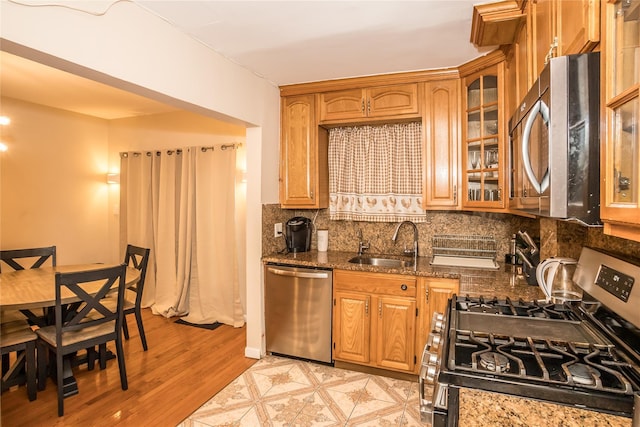 kitchen with a sink, appliances with stainless steel finishes, backsplash, dark stone countertops, and glass insert cabinets