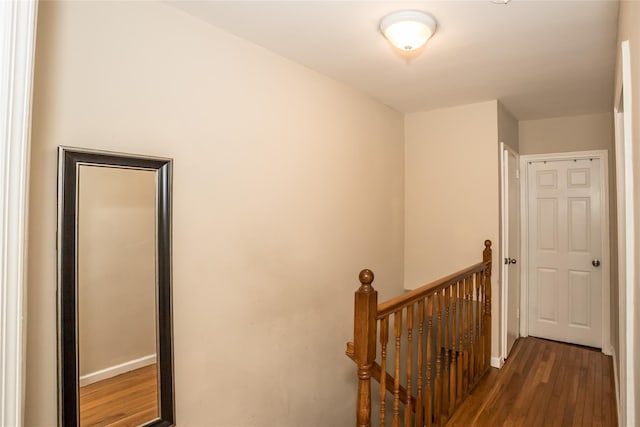 hallway with baseboards, an upstairs landing, and wood finished floors