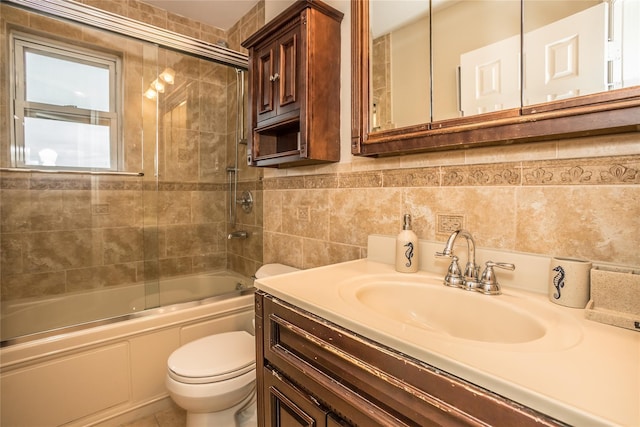 full bathroom featuring toilet, combined bath / shower with glass door, tile walls, and vanity