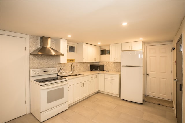 kitchen featuring white appliances, a sink, white cabinets, light countertops, and wall chimney range hood