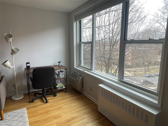 office space with radiator, a wall mounted air conditioner, and light wood-type flooring