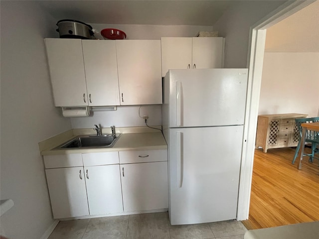 kitchen with white cabinetry, light hardwood / wood-style floors, sink, and white fridge