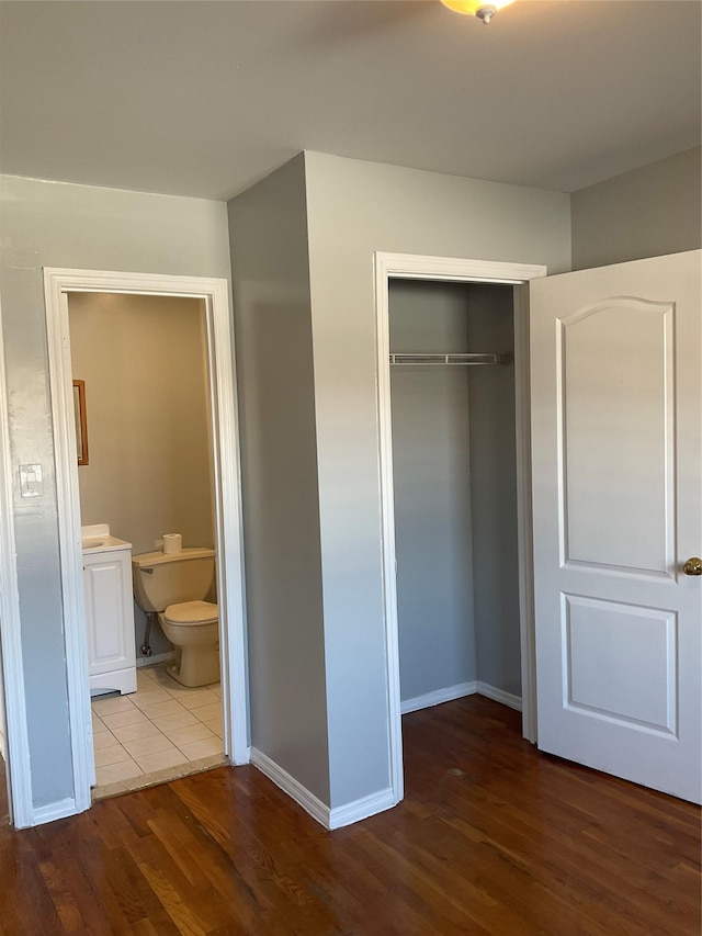 unfurnished bedroom featuring wood-type flooring, ensuite bathroom, and a closet