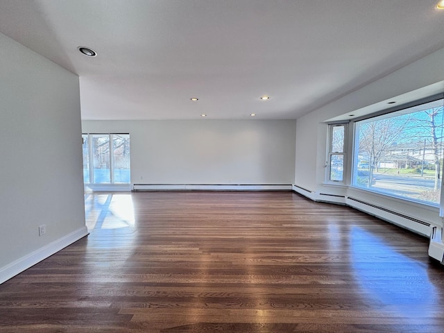 spare room featuring a baseboard heating unit and dark hardwood / wood-style flooring