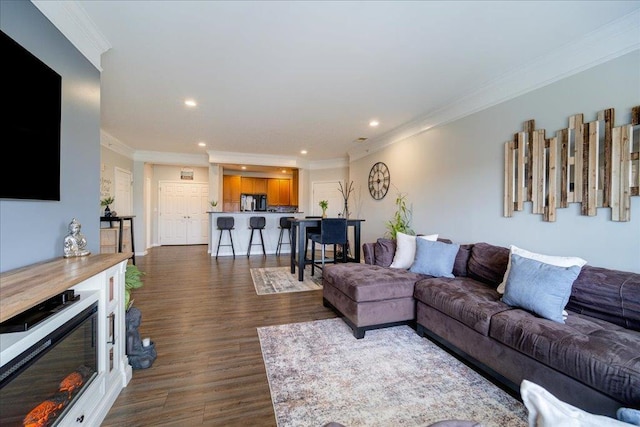 living room with dark wood-style floors, ornamental molding, a glass covered fireplace, and recessed lighting