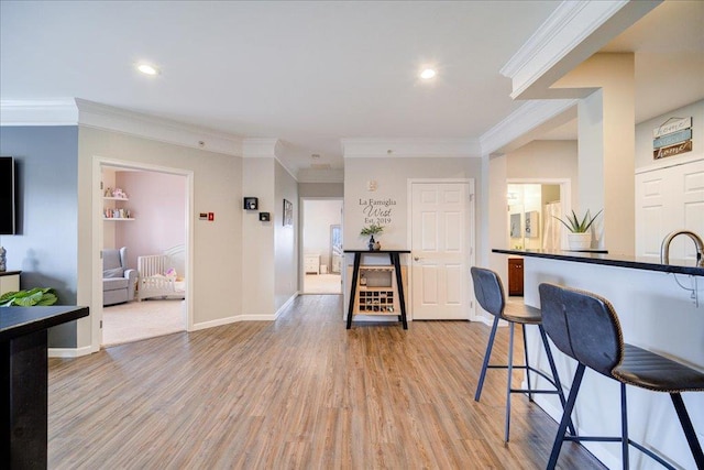 kitchen featuring light wood-type flooring, baseboards, a breakfast bar, and crown molding