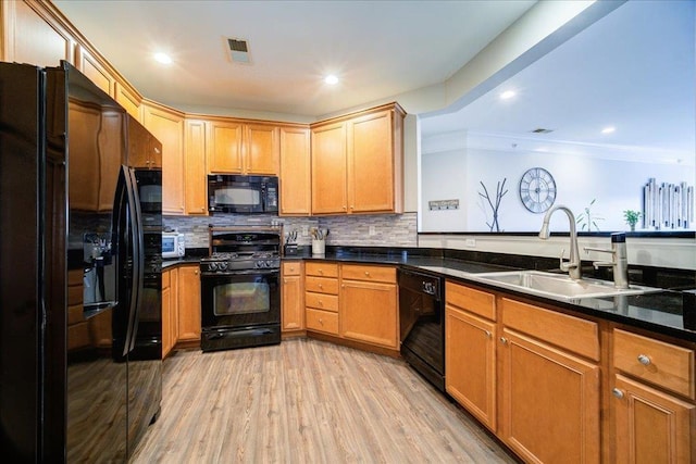 kitchen with black appliances, light wood-style flooring, decorative backsplash, and a sink