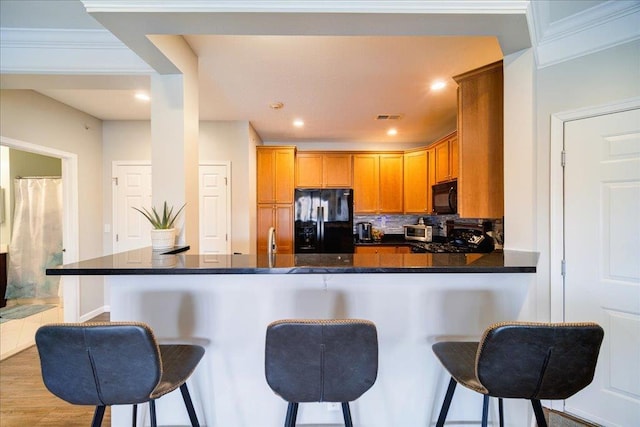 kitchen featuring tasteful backsplash, a breakfast bar, visible vents, and black appliances