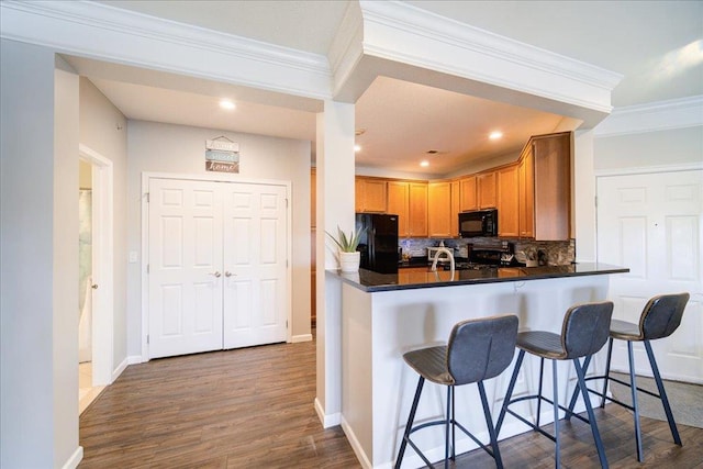 kitchen featuring a breakfast bar, dark wood finished floors, tasteful backsplash, ornamental molding, and black appliances