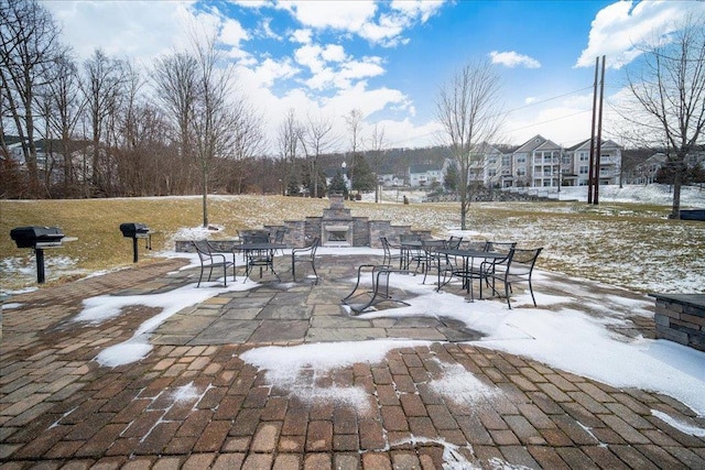 snow covered patio featuring an outdoor stone fireplace, a grill, and outdoor dining area