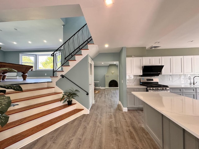 kitchen with gas stove, light wood-type flooring, a large fireplace, white cabinets, and backsplash