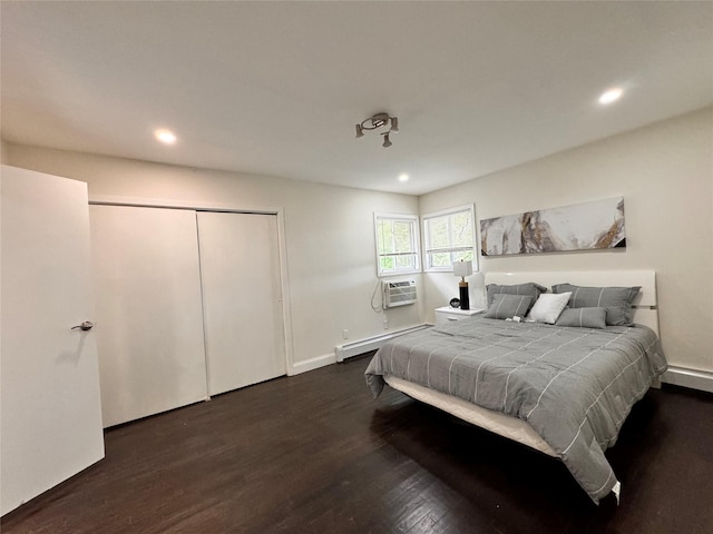 bedroom featuring a baseboard heating unit, dark wood-type flooring, a wall unit AC, and a closet