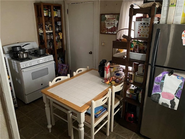 kitchen with white range with gas cooktop, dark tile patterned flooring, tile countertops, and stainless steel refrigerator