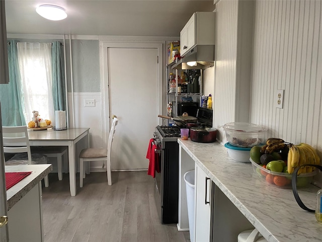 kitchen featuring white cabinetry, gas range, light stone countertops, and light wood-type flooring